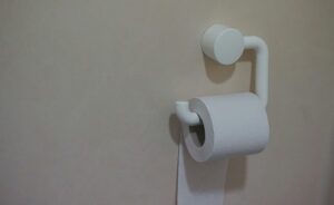 A simple white toilet paper holder mounted on a beige bathroom wall.